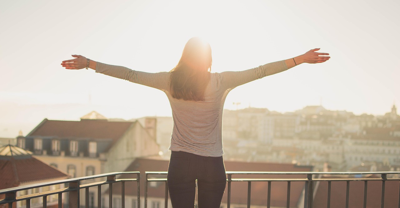 A person standing on a hill with arms wide open facing a golden sunset.