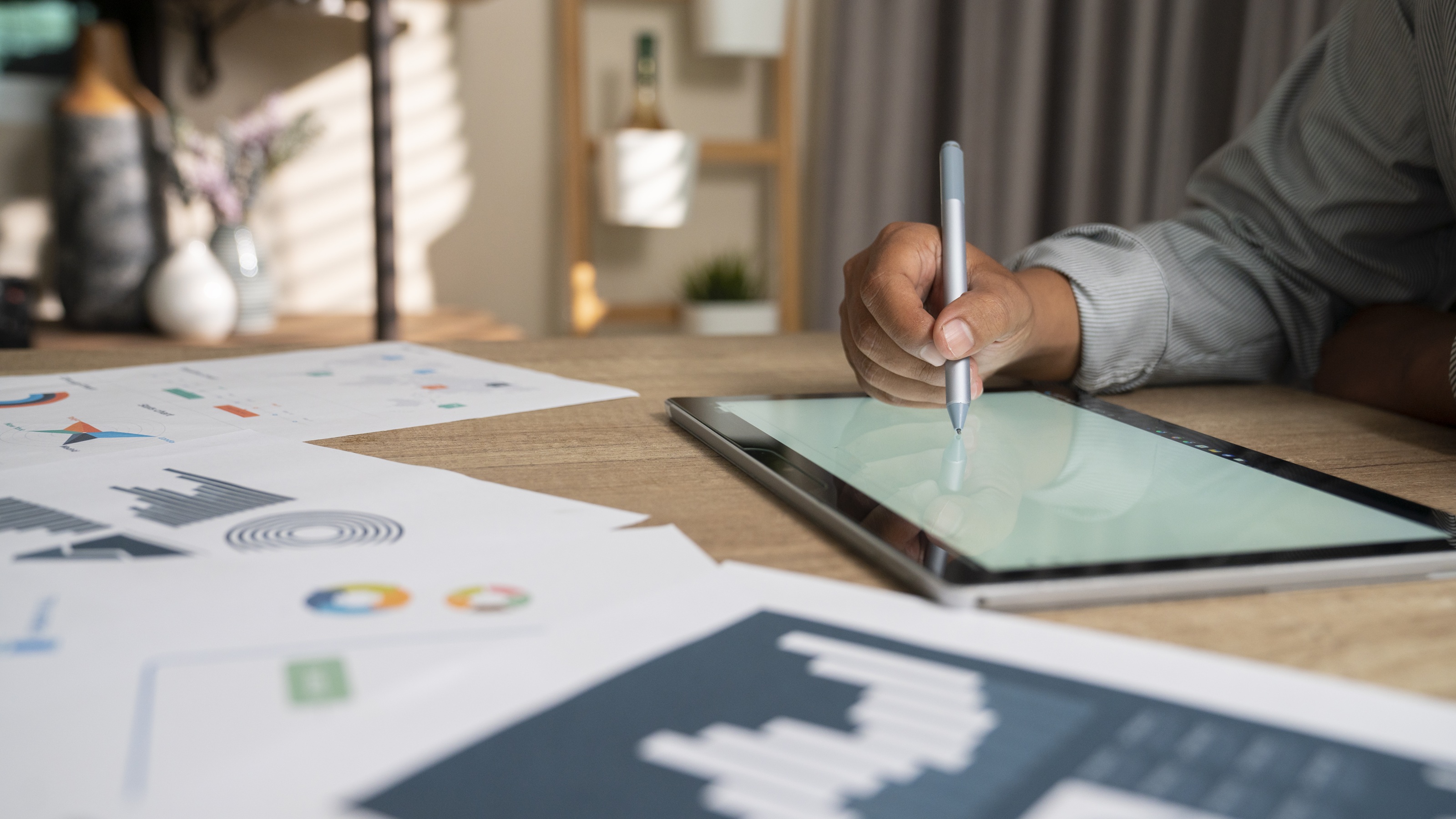 A person's hand managing financial charts and a portfolio on a desk with a digital tablet.