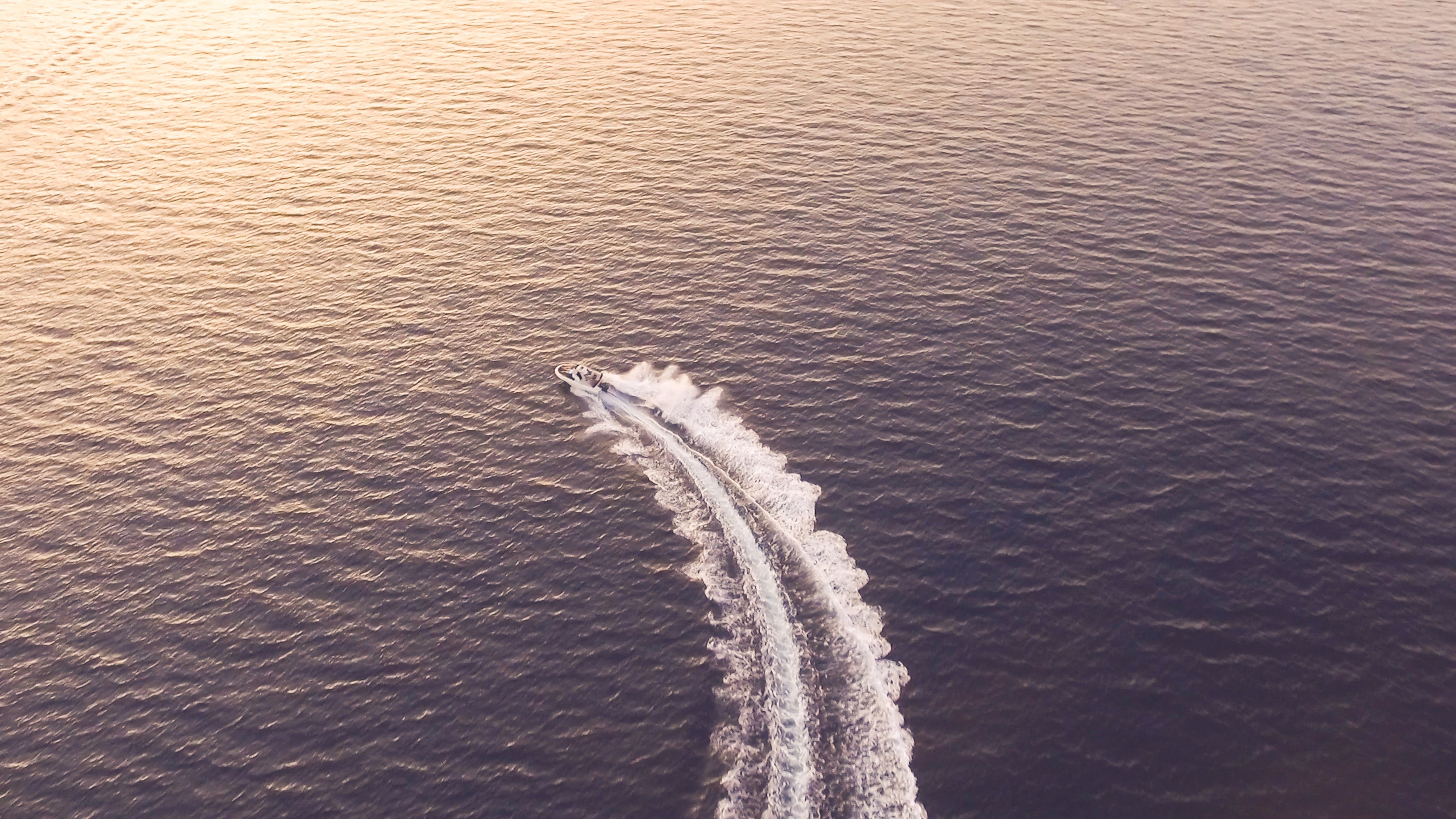 A boat heading towards a golden sunset on the water.