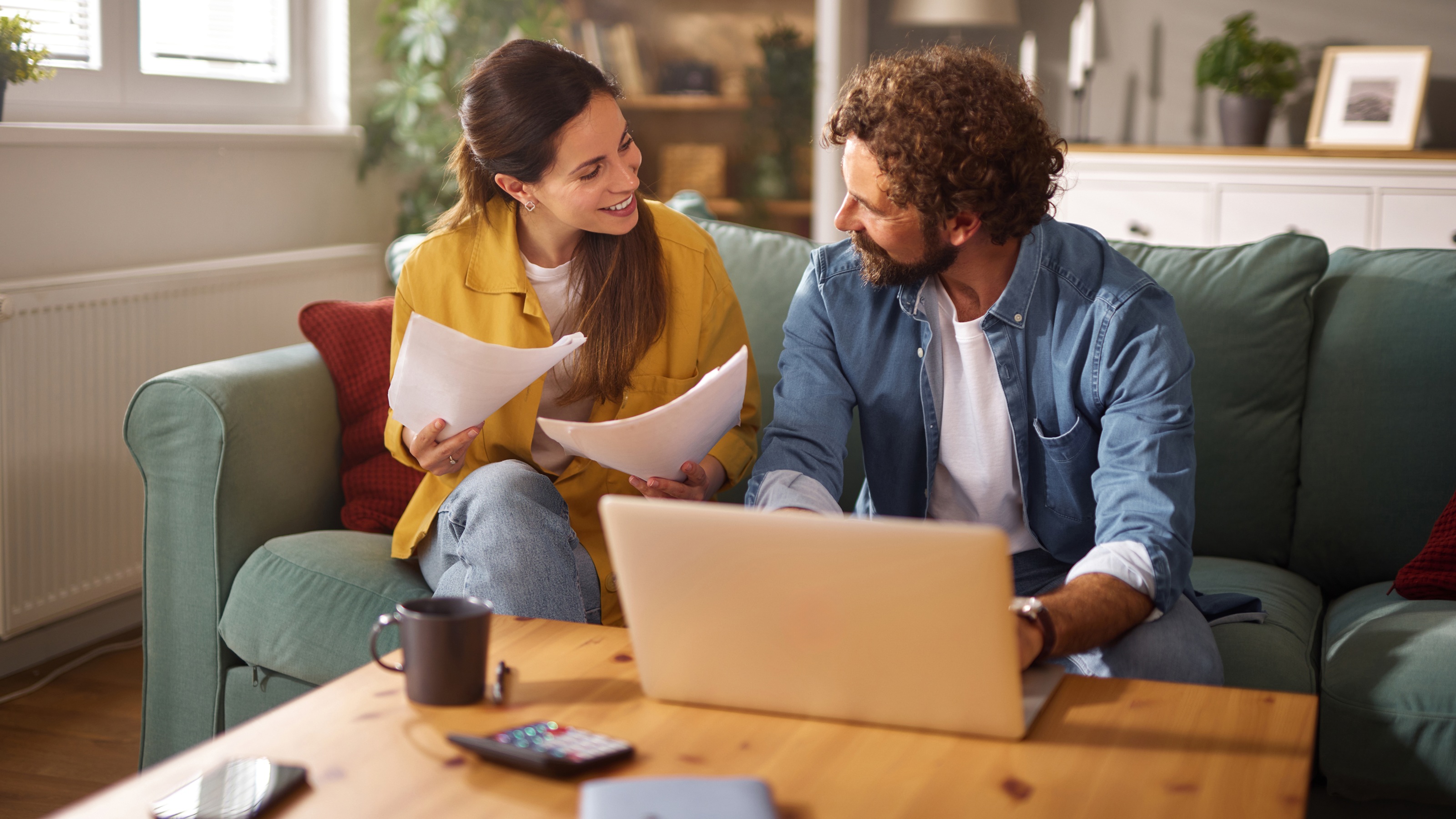 A couple reviewing financial documents and a laptop together on a sofa.