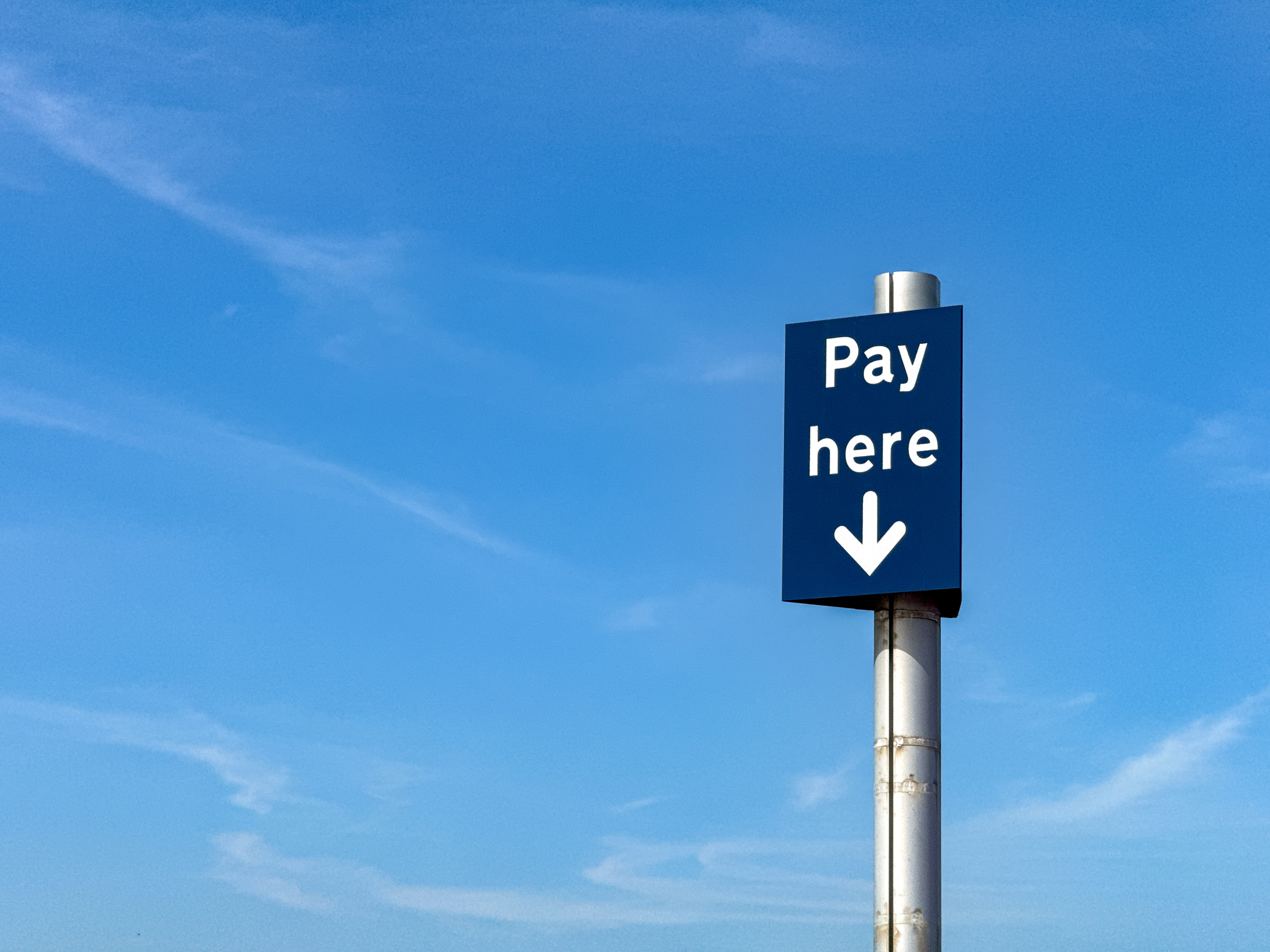 A 'Pay Here' sign against a blue sky, representing Medicare billing and mandatory surcharges.