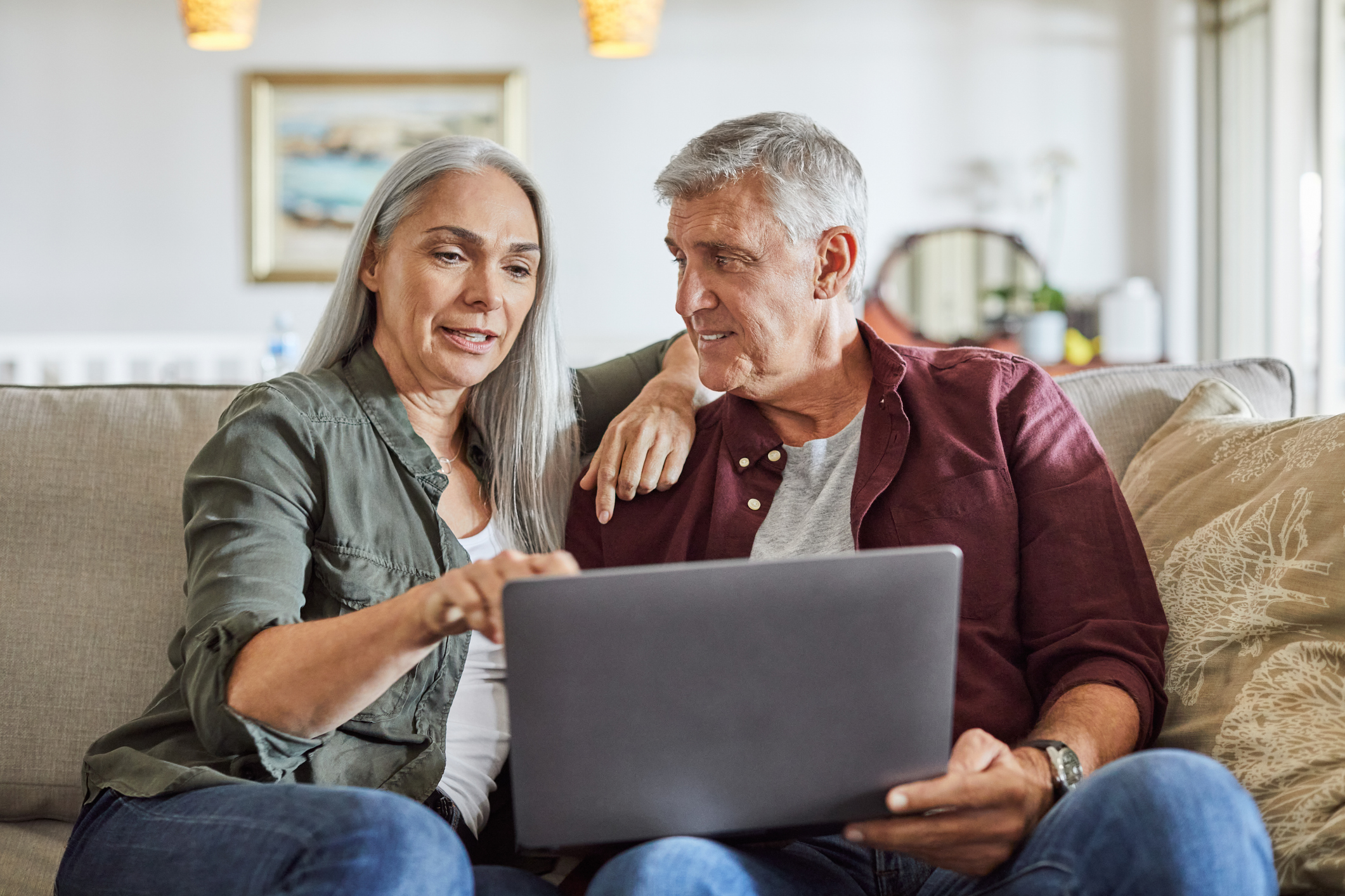 A mature man and woman smiling while looking at a laptop in their living room.