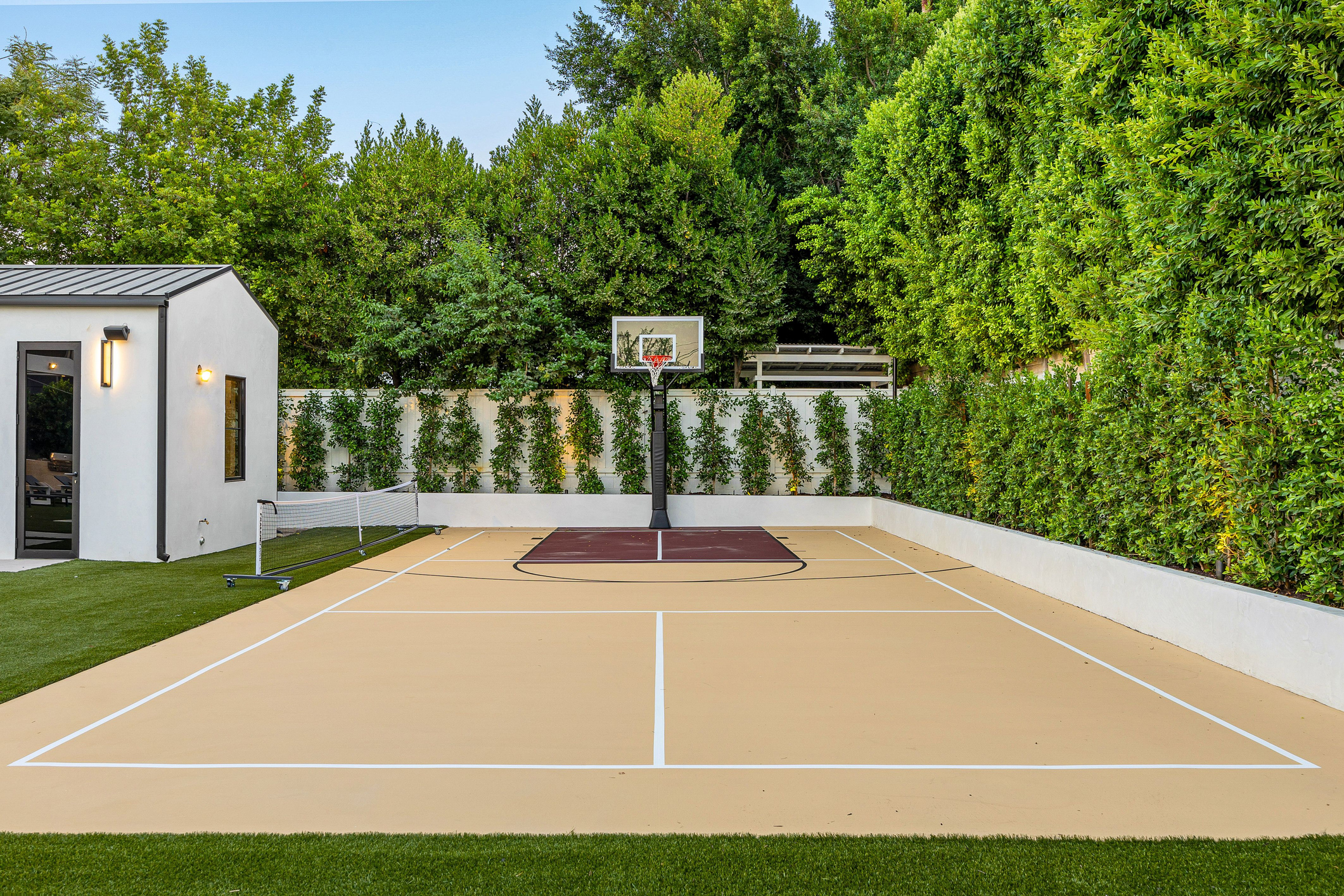 Modern backyard sports court with a basketball hoop and lush landscaping.