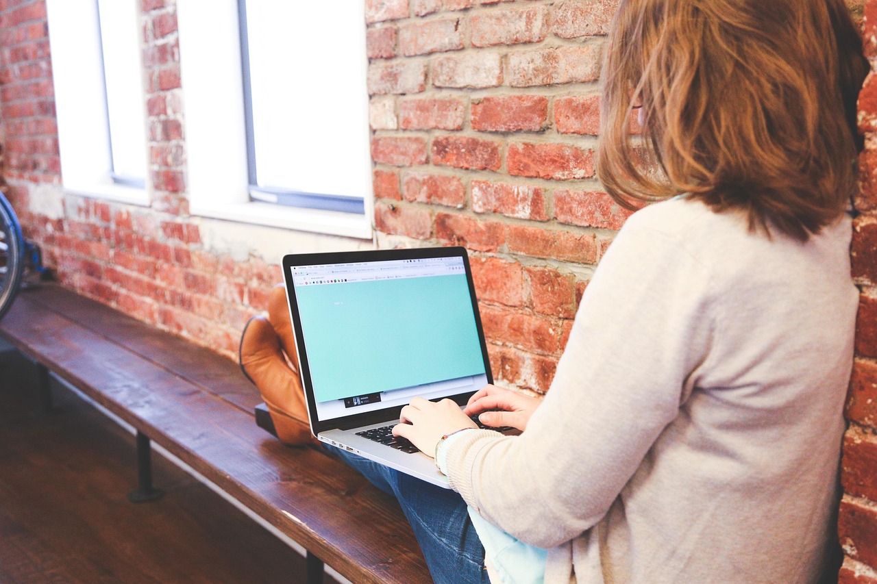 A professional woman using a calculator while working on a laptop in a bright office.
