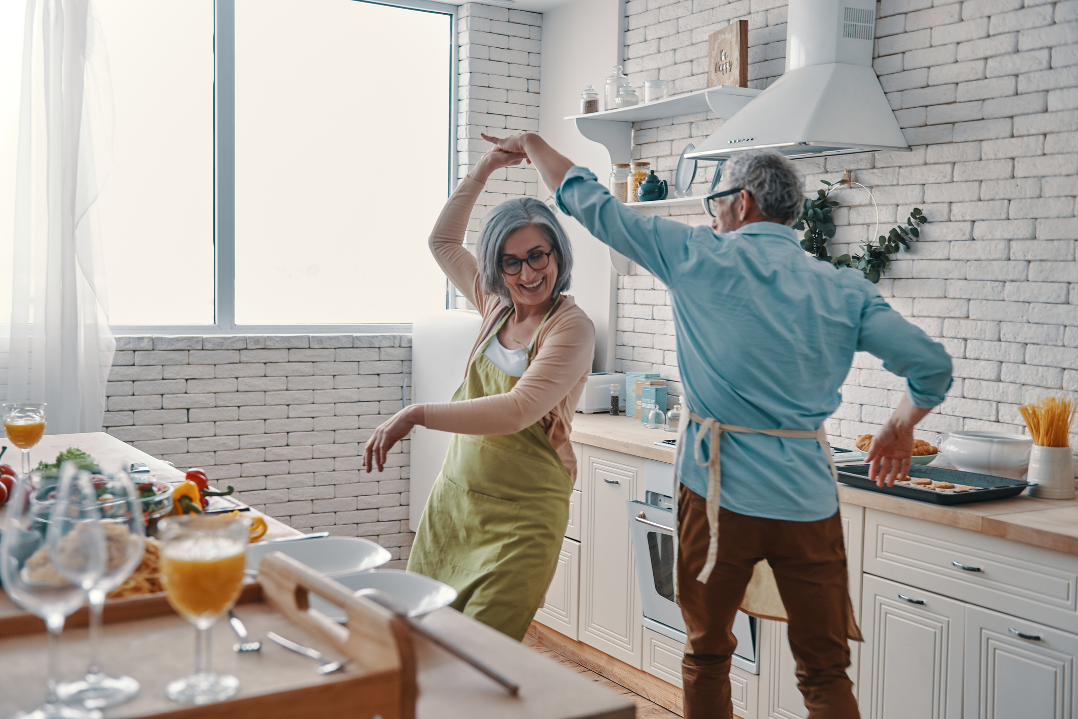 A joyful senior couple dancing and cooking together in their home kitchen.