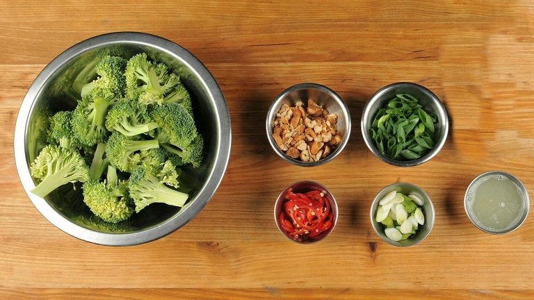 Top-down view of various pre-portioned stir fry ingredients including broccoli and peppers in small white bowls.