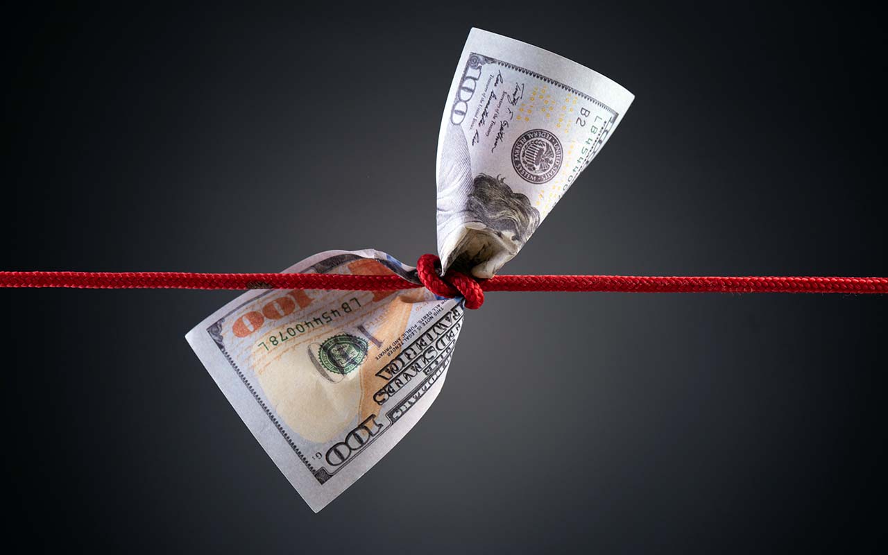 A dollar bill tied in a complex red knot signifying financial complications.