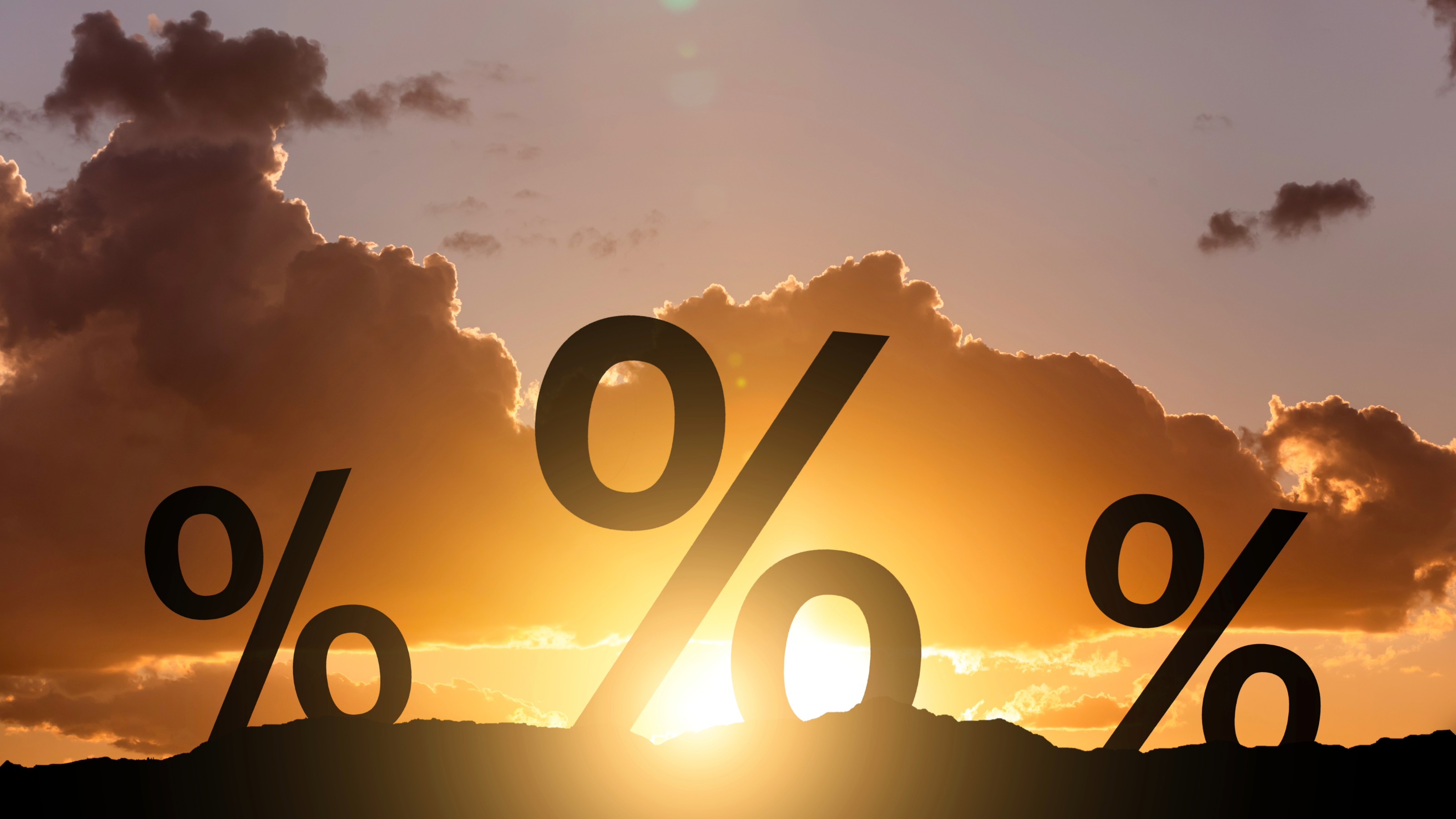 Percentage symbols silhouetted against a warm sunset, representing declining rates.