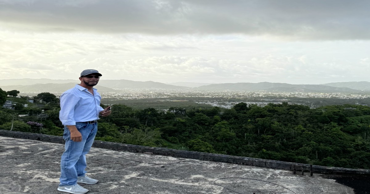 A man named Eric Rivera standing on the roof of his home with mountain views in Puerto Rico.