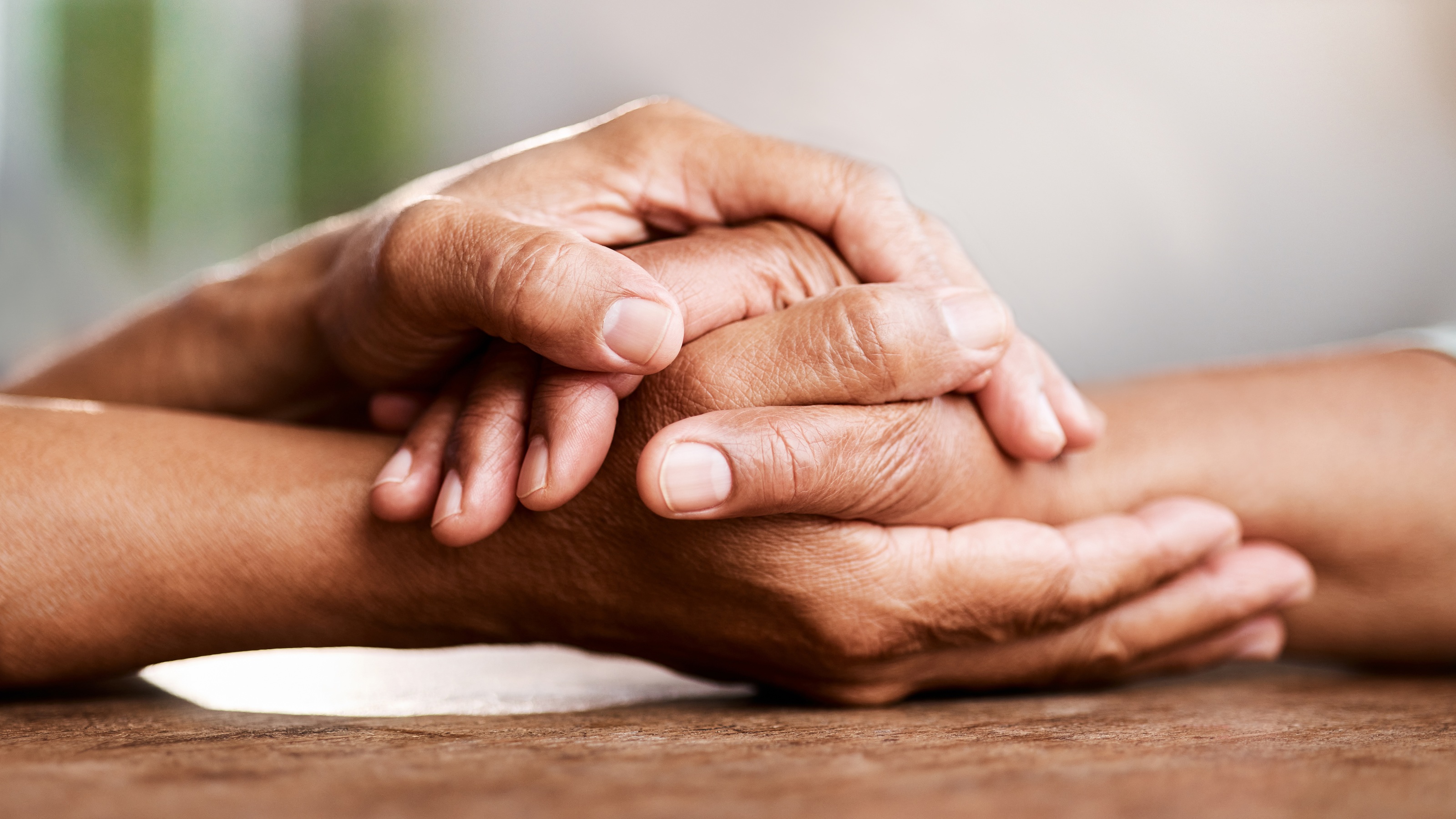 An older couple holding hands at a wooden table.