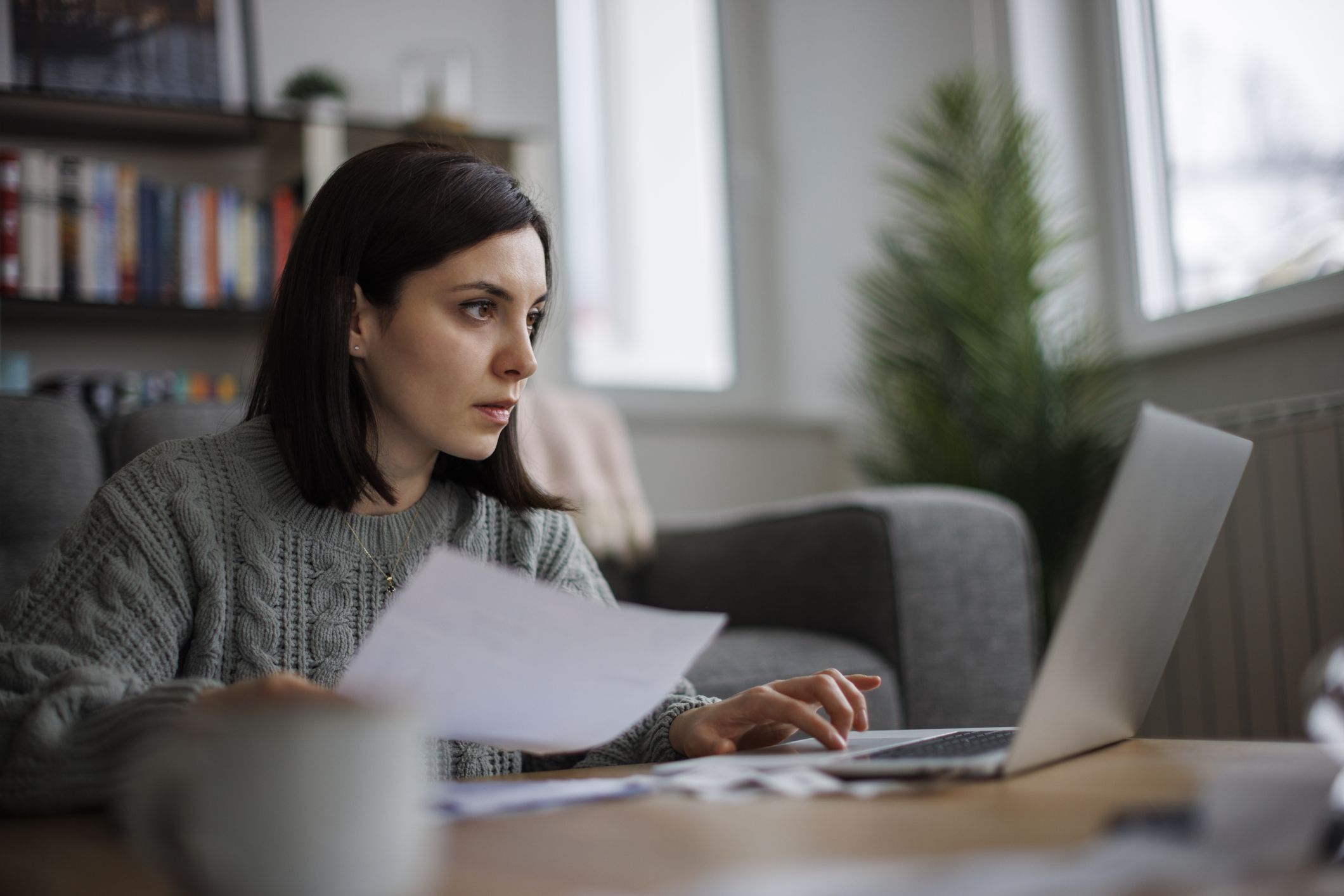 A professional woman at home reviewing financial documents and her retirement account on a laptop.