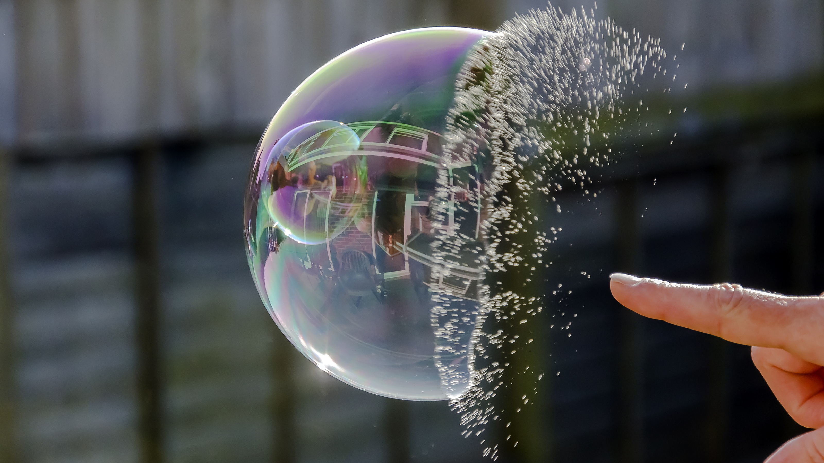 A close-up of a finger about to pop a large, glowing soap bubble.