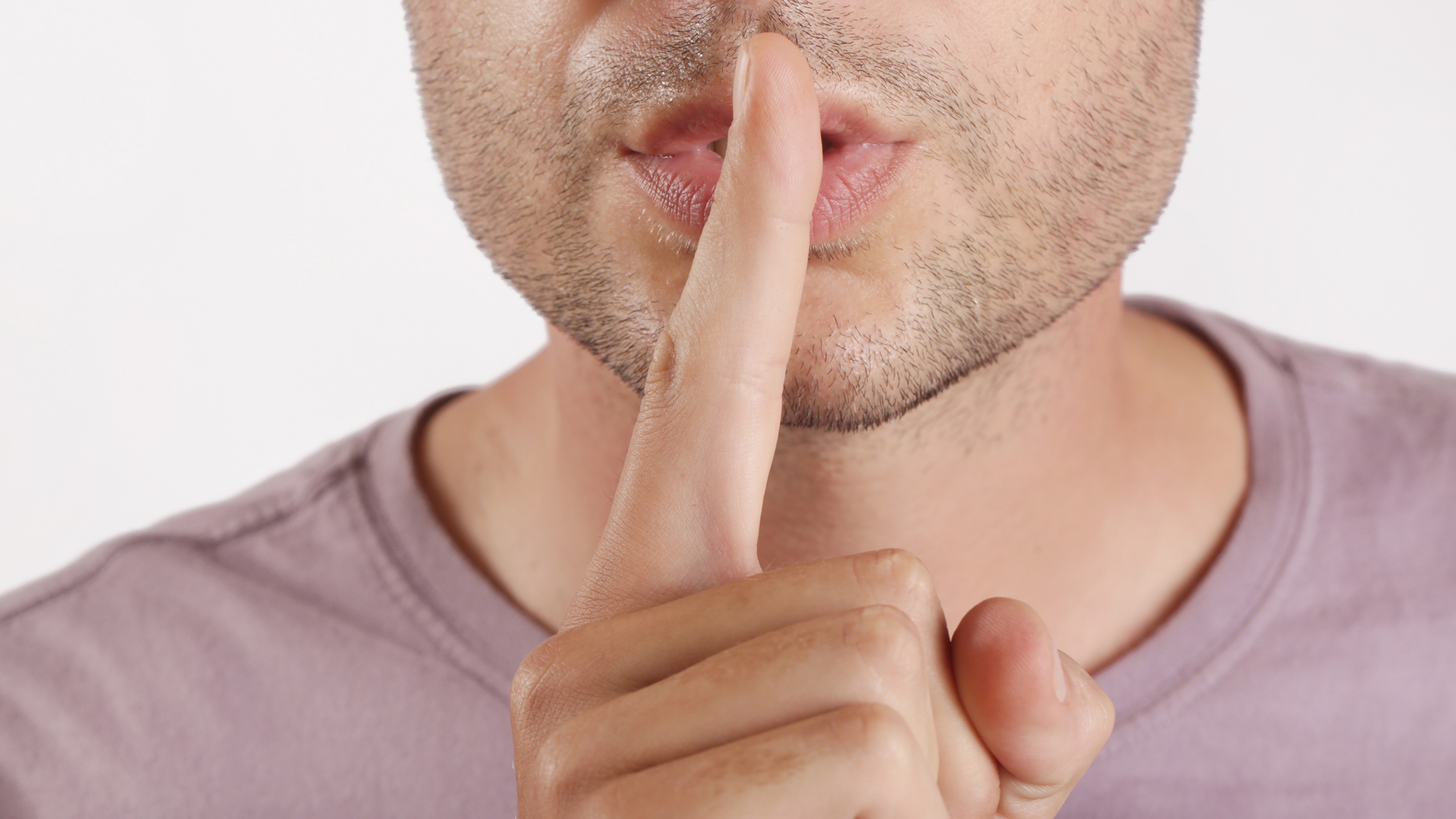 A close-up of a man making a quiet gesture by putting his finger to his lips.