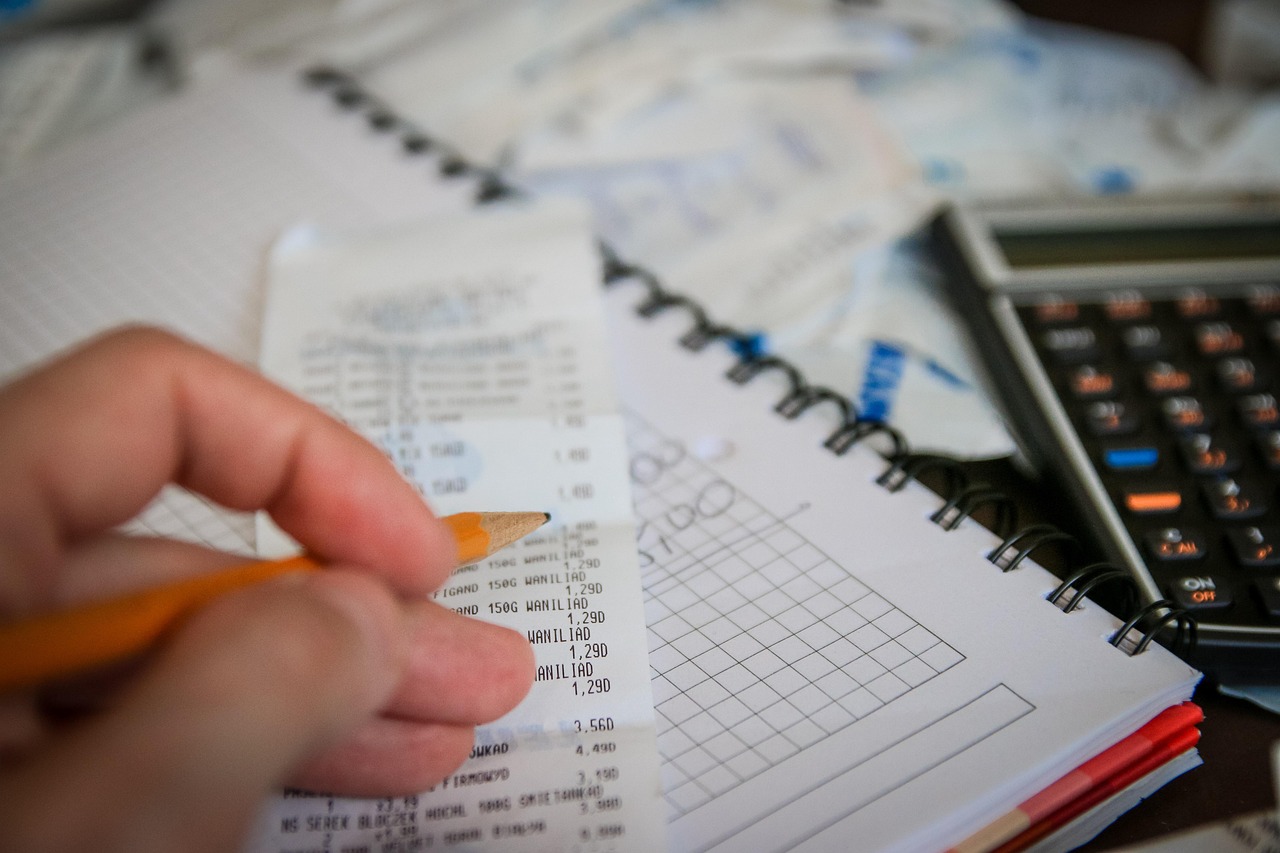 A notebook with a grocery list next to a calculator and some coins.