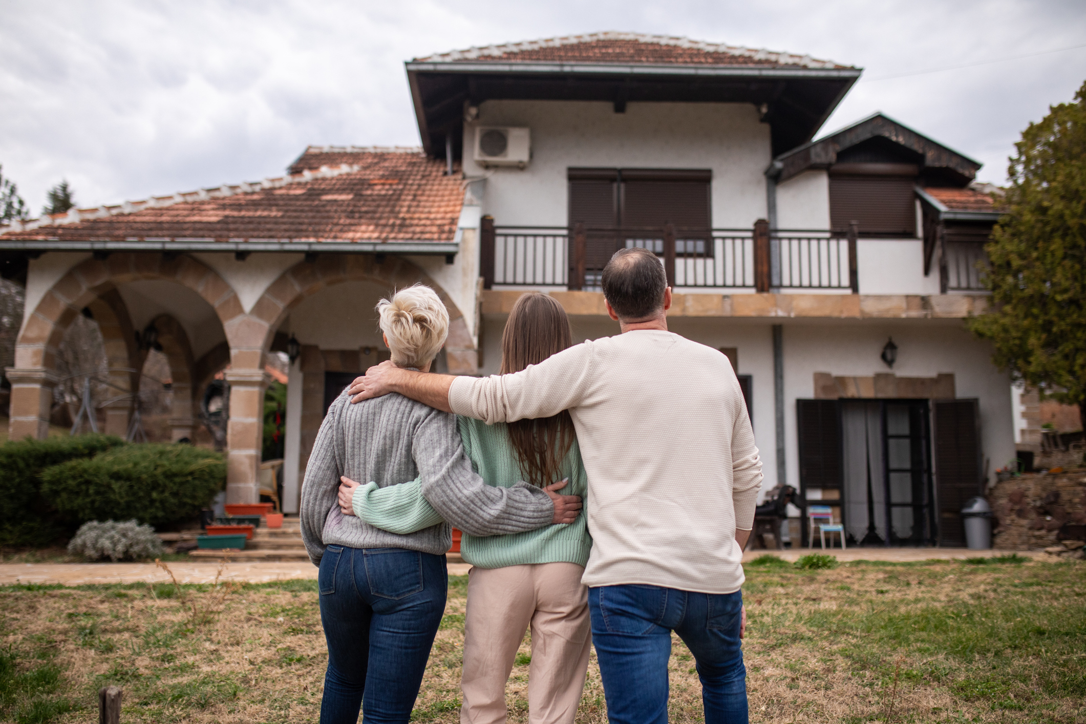 A family standing in front of a residential house smiling.