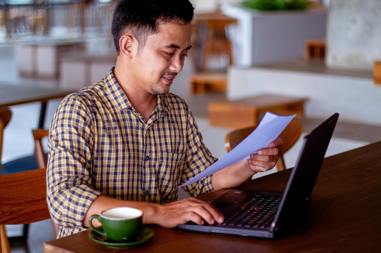 A young adult working on a silver laptop in a bright, modern indoor setting, representing the career transition.