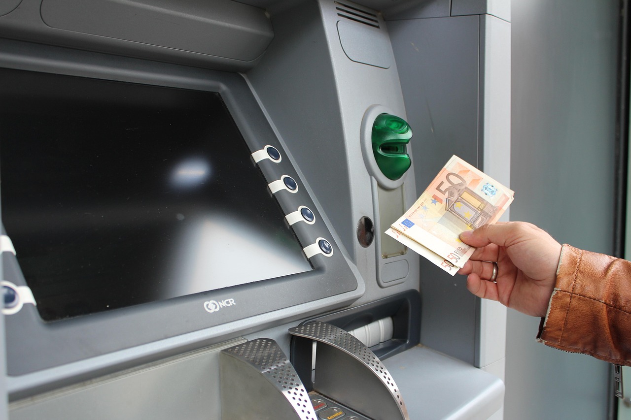 A person's hand taking cash out of an ATM machine in a brightly lit indoor area.
